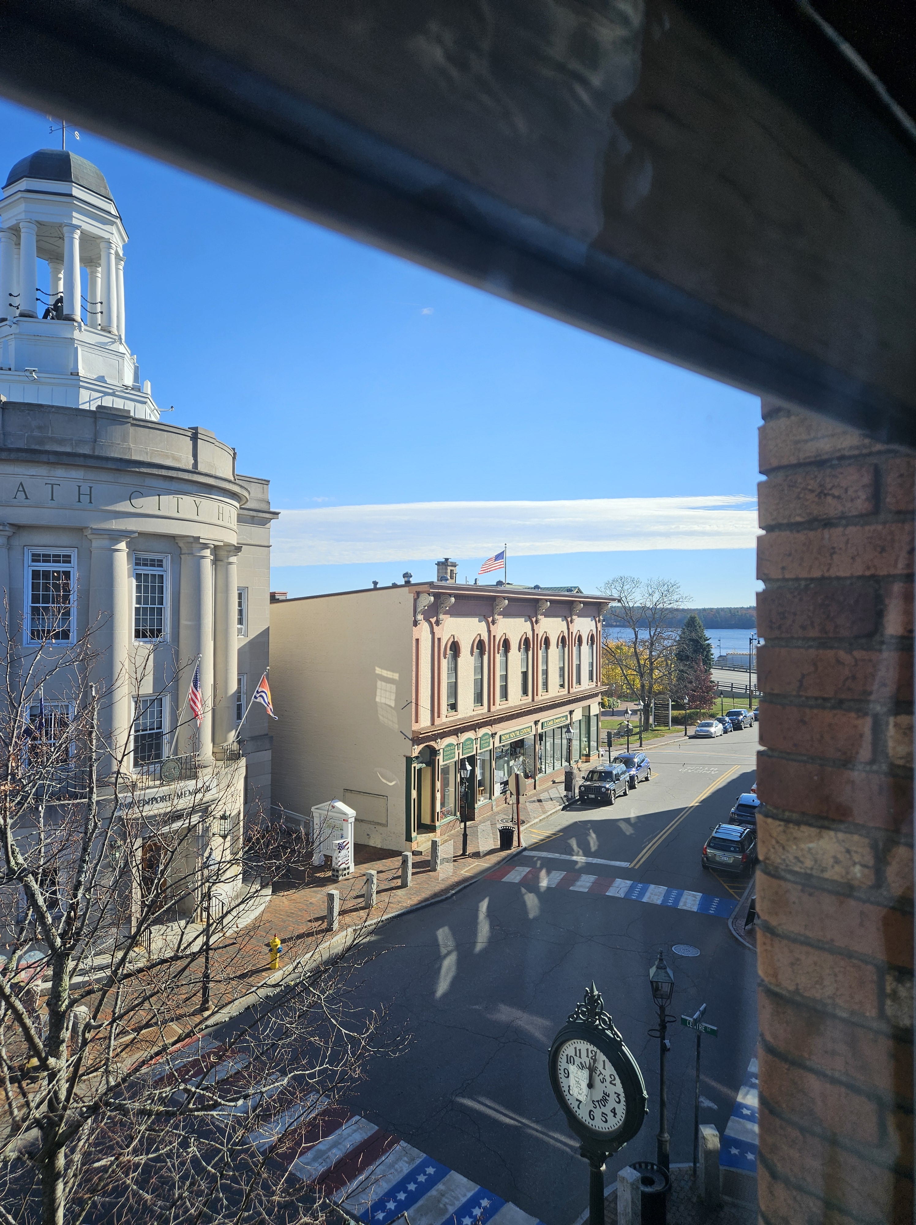 A view through a window in a brick building of Bath's city hall, part of the downtown street and blue sky.